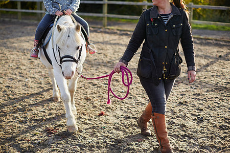 photos women wearing rubber boots - Instructor leading girl learning to ride pony in equestrian arena Foto de stock - Sin royalties Premium, Código: 649-09209425