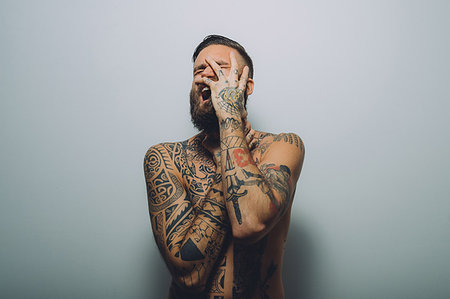 simsearch:6113-09199989,k - Portrait of young man with beard, covered in tattoos, hand on face, screaming Foto de stock - Sin royalties Premium, Código: 649-09212521