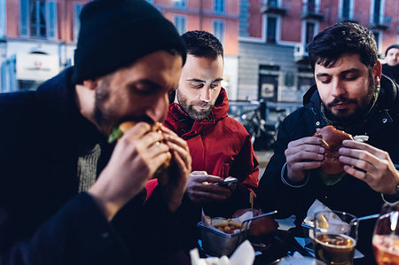 Friends enjoying burger at outdoor cafe, Milan, Italy Stock Photo - Premium Royalty-Free, Code: 649-09212567
