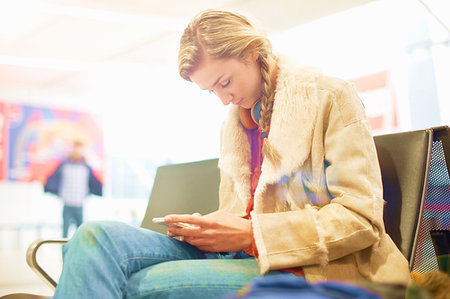 Young woman at airport, sitting, using smartphone Stock Photo - Premium Royalty-Free, Code: 649-09212651