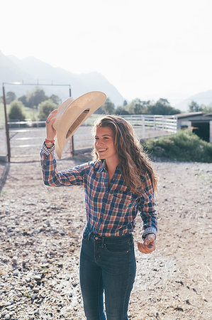 Cowgirl putting on stetson in rural equestrian arena Stock Photo - Premium Royalty-Free, Code: 649-09212946