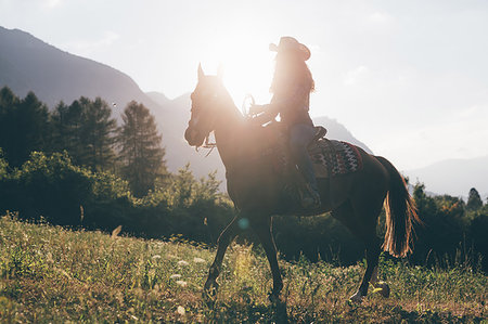 Cowgirl horse riding in field, backlit, Primaluna, Trentino-Alto Adige, Italy Stock Photo - Premium Royalty-Free, Code: 649-09212993