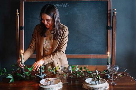 restaurant interior chalkboard - Young woman decorating vintage dinner table with candle and foliage Stock Photo - Premium Royalty-Free, Code: 649-09213117