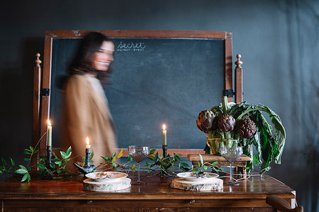 restaurant interior chalkboard - Young woman moving past vintage dinner table with candles and bowl of globe artichokes Stock Photo - Premium Royalty-Free, Code: 649-09213118
