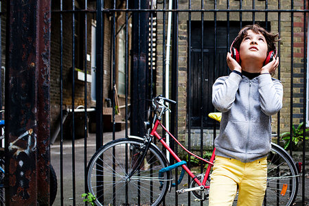 Boy listening to music with headphones, bicycle in background Photographie de stock - Premium Libres de Droits, Code: 649-09213488