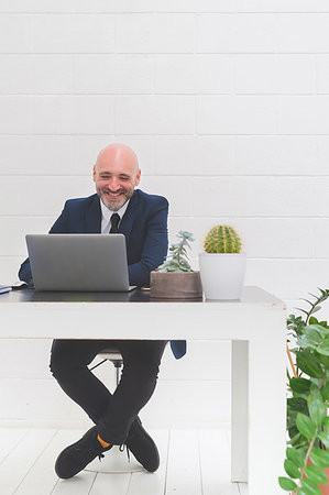 Businessman laughing while looking at laptop on office desk Foto de stock - Sin royalties Premium, Código: 649-09230623