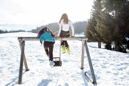 Two teenage girl skiers sitting on top of swing in snow covered landscape, rear view, Tyrol, Styria, Austria Stock Photo - Premium Royalty-Free, Code: 649-09257316