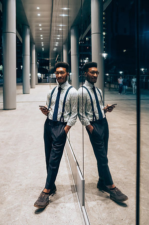 Businessman using smartphone, leaning against mirrored wall of office building, Milano, Lombardia, Italy Stock Photo - Premium Royalty-Free, Code: 649-09257419