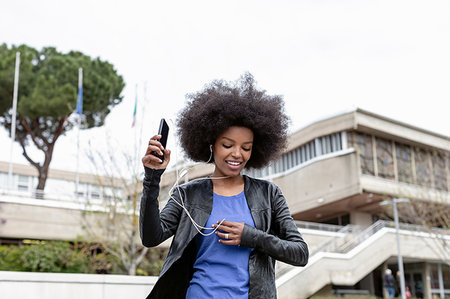 Young woman with afro hair in city, walking and listening to smartphone music Stock Photo - Premium Royalty-Free, Code: 649-09257701