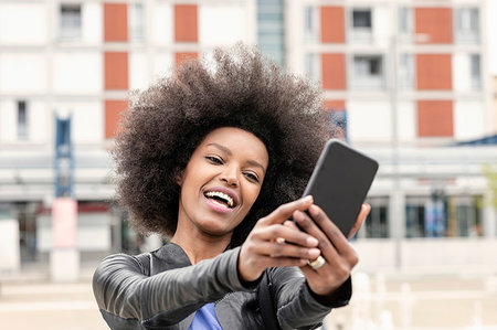 simsearch:649-09257703,k - Happy young woman with afro hair in city, taking smartphone selfie Foto de stock - Royalty Free Premium, Número: 649-09257711