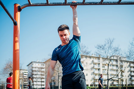 Calisthenics at outdoor gym, young man hanging by one arm from exercise equipment Stock Photo - Premium Royalty-Free, Code: 649-09257966