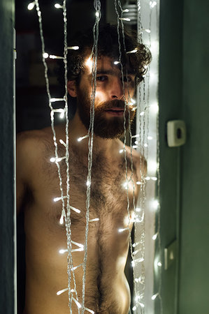 simsearch:649-09258330,k - Bearded young man standing behind string of decorative lights Stock Photo - Premium Royalty-Free, Code: 649-09258320