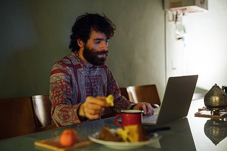 simsearch:649-09258330,k - Bearded young man having breakfast, using laptop at home Stock Photo - Premium Royalty-Free, Code: 649-09258331