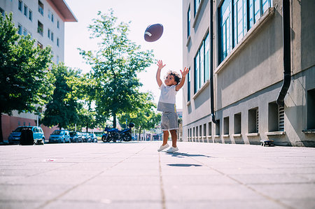 Toddler reaching up for rugby ball on sidewalk Stock Photo - Premium Royalty-Free, Code: 649-09250107