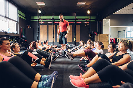 simsearch:6126-08644271,k - Large group of women training in gym with male trainer, sitting on floor with legs raised Stock Photo - Premium Royalty-Free, Code: 649-09268851