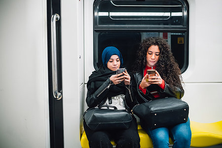 simsearch:614-08827048,k - Young woman in hijab and friend sitting on subway train looking at smartphones Foto de stock - Sin royalties Premium, Código: 649-09269049