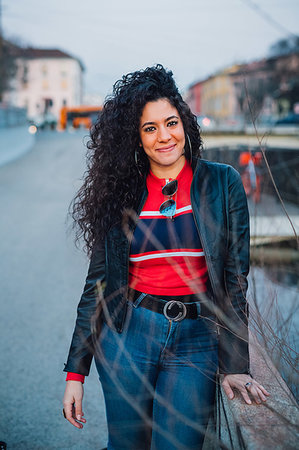 simsearch:614-08946703,k - Mid adult woman with long curly hair by city canal, portrait Photographie de stock - Premium Libres de Droits, Code: 649-09269092