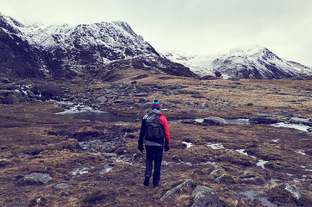 simsearch:649-08950376,k - Male hiker looking out at rugged landscape with snow capped mountains, rear view, Llanberis, Gwynedd, Wales Stock Photo - Premium Royalty-Free, Code: 649-09269115