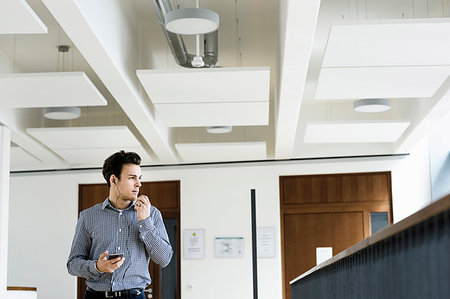 simsearch:649-09269443,k - Businessman using smartphone in office corridor Foto de stock - Royalty Free Premium, Número: 649-09269449