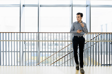 Businessman using smartphone in office corridor Stock Photo - Premium Royalty-Free, Code: 649-09269450