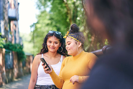 Young woman with teenage sisters looking at smartphone by park, over shoulder view Stock Photo - Premium Royalty-Free, Code: 649-09275621