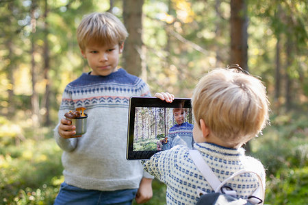 Toddler taking photograph of brother with cup of wild mushrooms in forest Stock Photo - Premium Royalty-Free, Code: 649-09277393