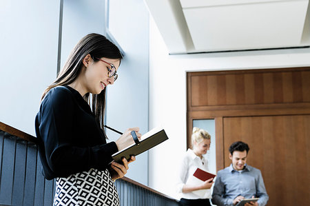 simsearch:614-07652551,k - Young businesswoman writing notes in office, colleagues talking in background Stock Photo - Premium Royalty-Free, Code: 649-09277643