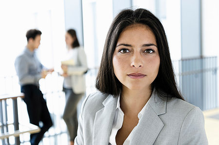 Young businesswoman in office, colleagues talking in background Stock Photo - Premium Royalty-Free, Code: 649-09277653