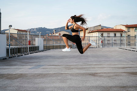 simsearch:693-05552869,k - Young woman doing jumping lunges on rooftop deck Stock Photo - Premium Royalty-Free, Code: 649-09277702