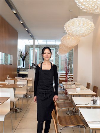 Young waitress standing in empty restaurant, smiling, portrait Stock Photo - Premium Royalty-Free, Code: 649-01557487