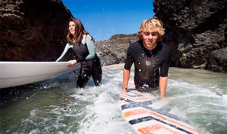 simsearch:649-01695983,k - Couple standing in water with surfboards smiling. Fotografie stock - Premium Royalty-Free, Codice: 649-01695906