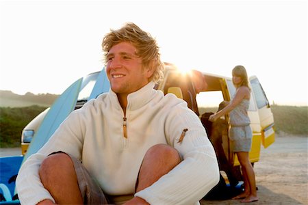 simsearch:649-01695983,k - Man sitting on beach smiling with woman unloading van at the beach . Fotografie stock - Premium Royalty-Free, Codice: 649-01695941