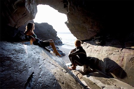 simsearch:649-01695983,k - Couple sitting on large rocks in wetsuits. Fotografie stock - Premium Royalty-Free, Codice: 649-01696019
