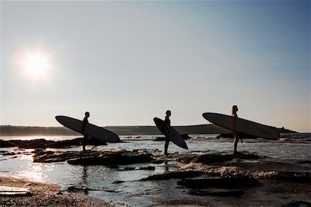 Three people holding surfboards standing on large rocks. Stock Photo - Premium Royalty-Free, Code: 649-01696093