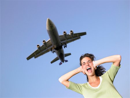 Woman covering ears and screaming with plane flying overhead. Stock Photo - Premium Royalty-Free, Code: 649-01696463