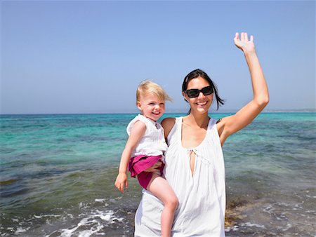 Woman holding a young girl at the beach waving and smiling. Stock Photo - Premium Royalty-Free, Code: 649-01696524