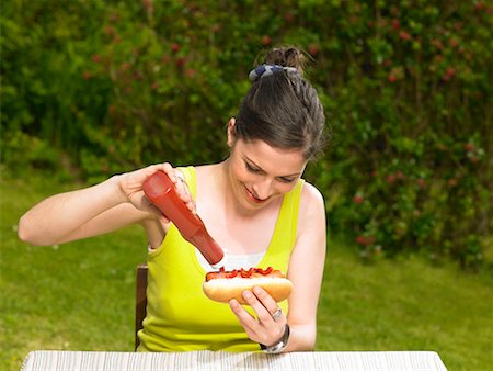 Young woman pouring ketchup onto hot dog Foto de stock - Royalty Free Premium, Número: 649-02290558