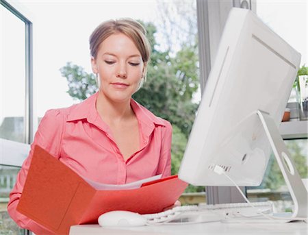 escritorio (pantalla del monitor) - Female looking in a folder at her desk Foto de stock - Sin royalties Premium, Código: 649-02423445