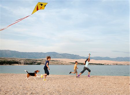 running on beach with dog - Children flying kite at beach Stock Photo - Premium Royalty-Free, Code: 649-03511054