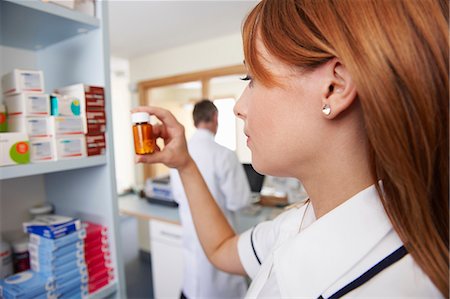 reaching for shelf - Pharmacist looking at pills in bottle Stock Photo - Premium Royalty-Free, Code: 649-03621591