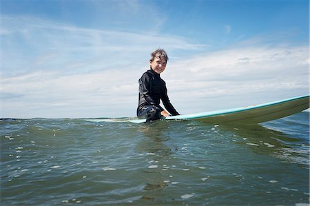 Young boy sitting on surf board at sea Stock Photo - Premium Royalty-Free, Code: 649-03768920