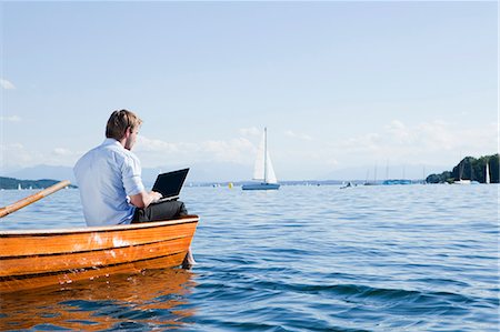 Man sitting on a rowboat using laptob Stock Photo - Premium Royalty-Free, Code: 649-03770468