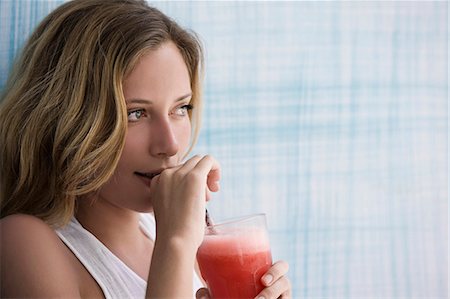 Girl drinking red smoothie, up against blue wall Stock Photo - Premium Royalty-Free, Code: 649-03797431