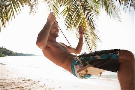 Homme souriant, se balancer sur une plage tropicale Photographie de stock - Premium Libres de Droits, Code: 649-03881282