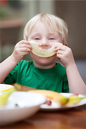 Boy playing with slice of melon at table Stock Photo - Premium Royalty-Free, Code: 649-03882692