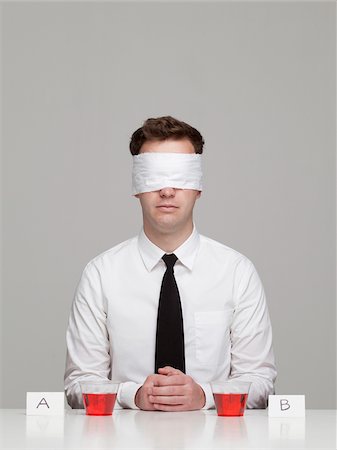 Studio portrait of young man with blindfold sitting in front of two glasses with red liquid Stock Photo - Premium Royalty-Free, Code: 640-05761249