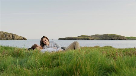 simsearch:640-09013423,k - Smiling boyfriend and girlfriend laying in grassy field near lake in remote landscape under blue sky Photographie de stock - Premium Libres de Droits, Code: 640-09013373