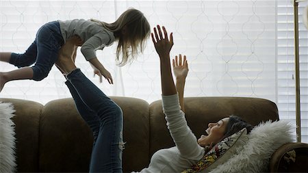 simsearch:693-03363809,k - Profile of laughing playful mother lifting daughter in mid-air and playing on sofa Stock Photo - Premium Royalty-Free, Code: 640-09013397