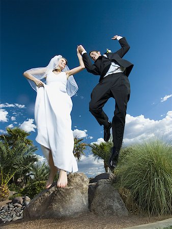 Low angle view of a newlywed couple holding hands and jumping Stock Photo - Premium Royalty-Free, Code: 640-01348725