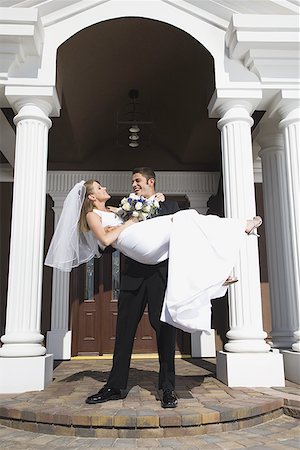 Young man carrying his bride in his arms in front of a building Stock Photo - Premium Royalty-Free, Code: 640-01349214